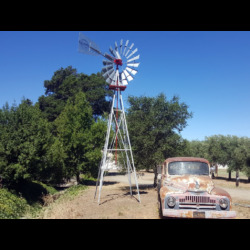 Which is older, the truck or the windmill? windmill and tower next to old truck